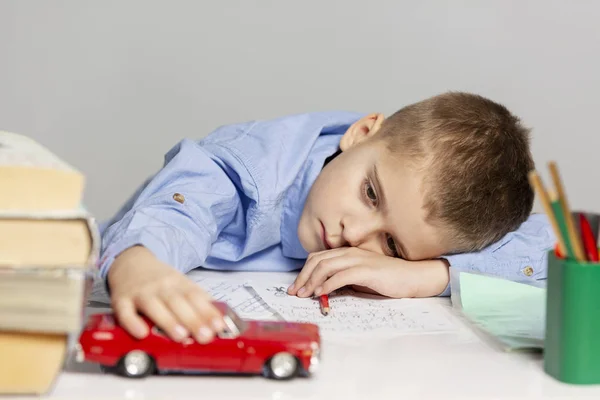 Schattige moe jongen doet huiswerk op de tabel, grijze achtergrond — Stockfoto