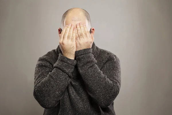 Homem careca cobriu o rosto com as mãos, fundo cinza — Fotografia de Stock