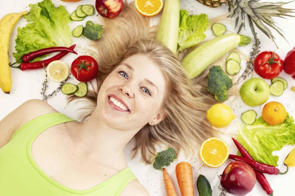 Young smiling woman lies in fruits and vegetables — Stock Photo, Image