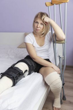 Bacağında bir işlem yatakta oturuyor sonra üzgün kadın. 
