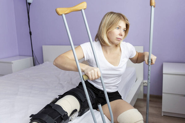 Sad woman after an operation on her leg is sitting on the bed.