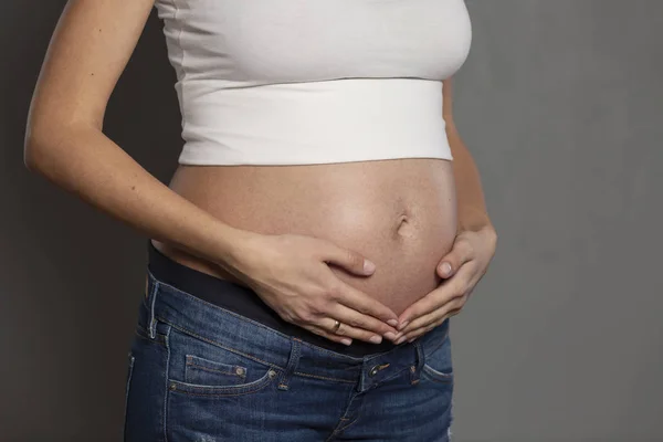La pancia di una donna incinta. Periodo 6 mesi, primo piano. Fondo grigio — Foto Stock