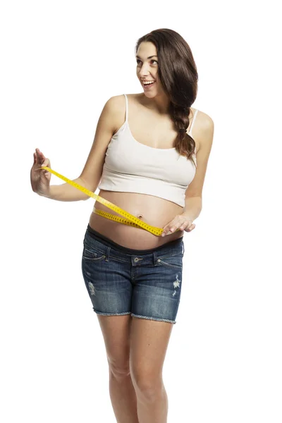 En gravid kvinna mäter bukens omkrets. Isolerad på en vit bakgrund. — Stockfoto