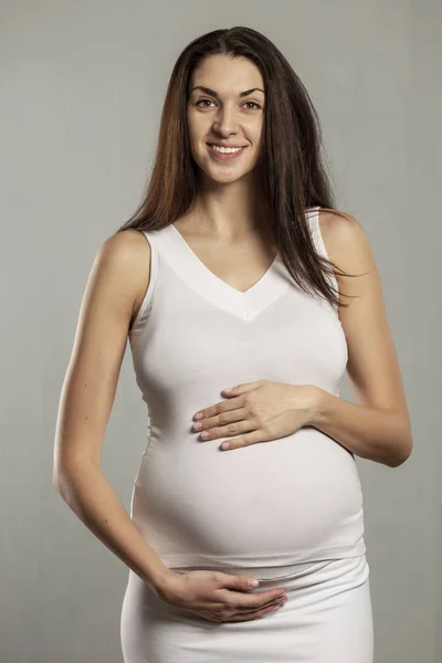 Young beautiful pregnant woman gently hugs belly and smiles — Stock Photo, Image