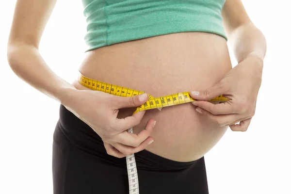 En gravid kvinna mäter buken omkrets. Sen period av graviditet. Närbild. Isolerad på en vit bakgrund. — Stockfoto