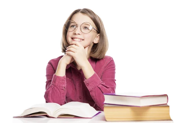 Gözlüklü gülümseyen genç bir kız kitapları olan bir masada oturuyor. Beyaz arka planda yalıtılmış. — Stok fotoğraf