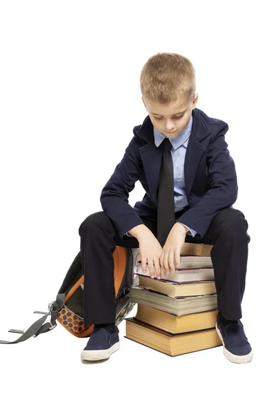 Triste colegial con un traje sentado en un montón de libros, la cabeza inclinada. Aislado sobre un fondo blanco . —  Fotos de Stock