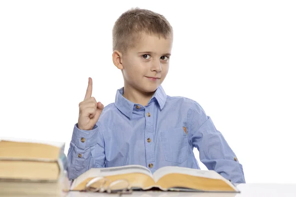 Leuke lachende school jongen zittend aan de tafel met lessen. Geïsoleerd op een witte achtergrond. — Stockfoto