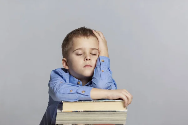 Schattige school jongen slaapt op een stapel boeken. Close-up. Grijze achtergrond. — Stockfoto