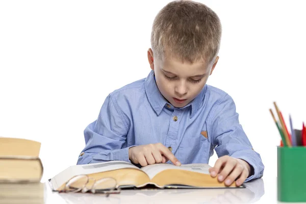 De school jongen zit aan tafel en doet zijn huiswerk. Geïsoleerd op een Whie achtergrond. — Stockfoto