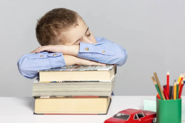 Schoolboy sover på böckerna för att göra läxor. Närbild. Grå bakgrund. — Stockfoto