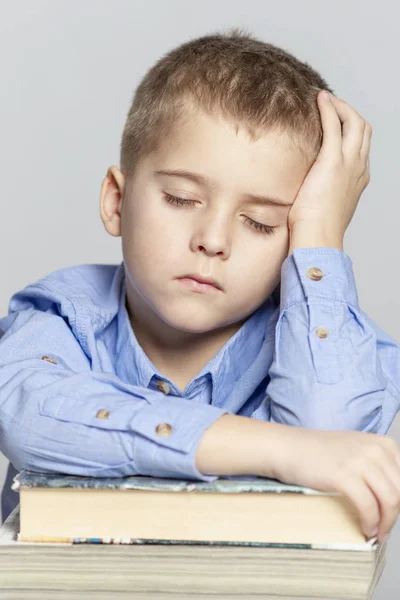 Schoolboy sover på böckerna för att göra läxor. Närbild. Grå bakgrund. — Stockfoto