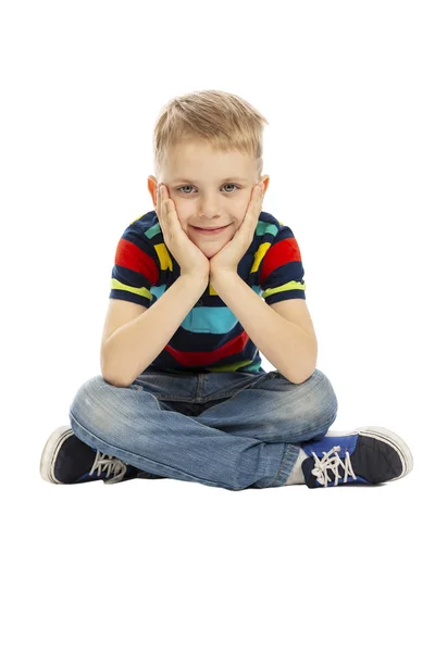 Un niño con una camiseta brillante está sentado en el suelo y sonriendo. Aislado sobre un fondo blanco . — Foto de Stock