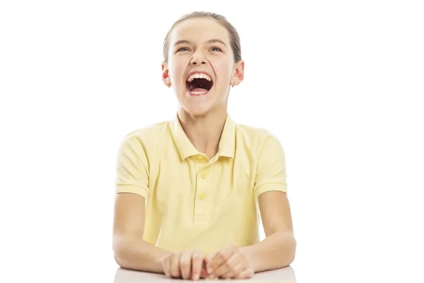 Dívčí teenager sedí u stolu a směje se. Izolováno na bílém pozadí. — Stock fotografie