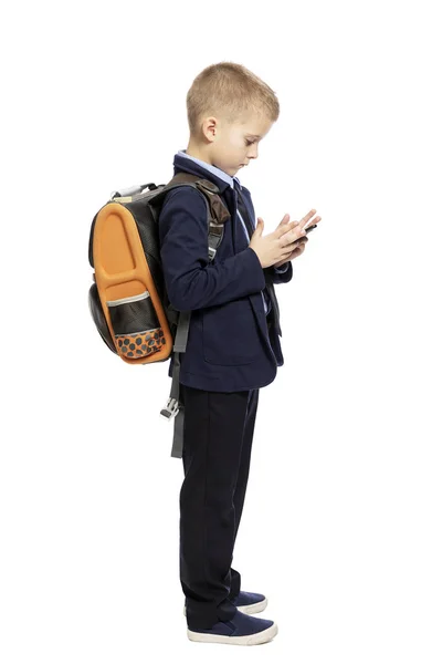 Školák v obleku s batohu a smartphone v dlaních. Izolováno na bílém pozadí. — Stock fotografie