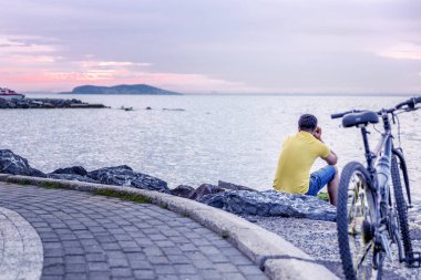 Bisikletçi gün batımında sahilde oturur
