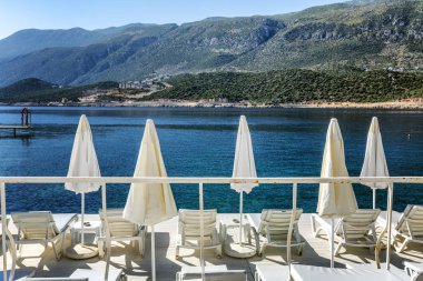 Dağların ve mavi denizin arkaplanına karşı güzel bir koyda beyaz şezlonglar. Lüks tatil köyü.