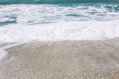 Kumlu plajda köpüklü turkuaz deniz dalgası. Yakın çekim, arka plan. Metin alanı.