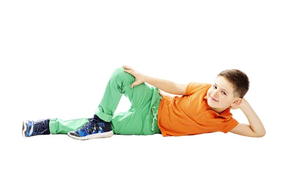 Een lachende schooljongen in een oranje T-shirt is liggend op zijn kant. Geïsoleerd op een witte achtergrond. — Stockfoto