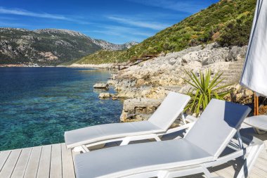 Şeffaf denizin kıyısında şemsiyeli beyaz şezlong. Kalmak için lüks bir yer.