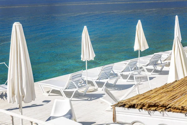 透明な海の岸に傘が付いている白いラウンジチェア。豪華な宿泊先. — ストック写真