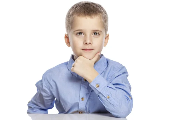 Lindo chico serio de la edad escolar se sienta a la mesa. Aislado sobre un fondo blanco . — Foto de Stock