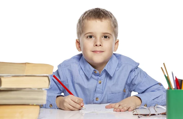 Söt pojke i skolåldern gör läxor vid bordet. Det är intressant att lära. Isolerad på en vit bakgrund. — Stockfoto