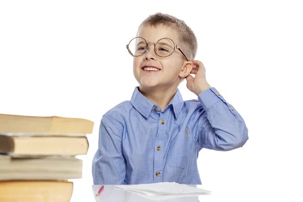Aranyos fiú a pohár iskolás korú csinál házi feladatot az asztalnál, és nevetve. Érdekes megtanulni. Fehér alapon izolált. — Stock Fotó