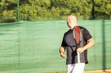 Orta yaşlı kel bir adam sahada duygusal olarak tenis oynar. Rakibi kaybeder. Açık.