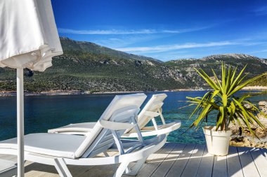 Beyaz şezlong ile güzel bir koyda lüks plaj. Güneşli bir günde denizin ve dağların muhteşem manzarası.