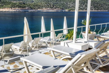 Beyaz şezlong ile güzel bir koyda lüks plaj. Güneşli bir günde denizin ve dağların muhteşem manzarası.