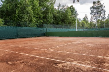 Güneşli bir günde doğal toprak yüzeyi ile boş tenis kortu.