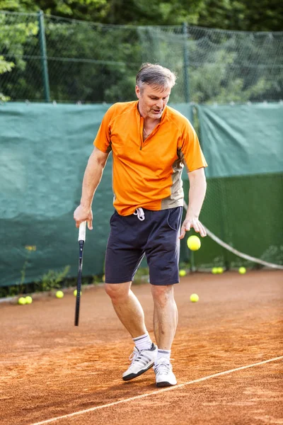 Orta yaşlı bir adam güneşli bir yaz gününde doğal toprak yüzeyi olan bir kortta tenis oynar.. 