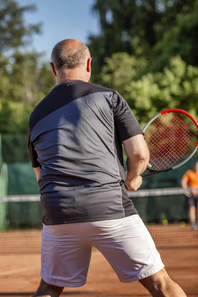 Homem careca adulto joga tênis na quadra. Dia ensolarado . — Fotografia de Stock