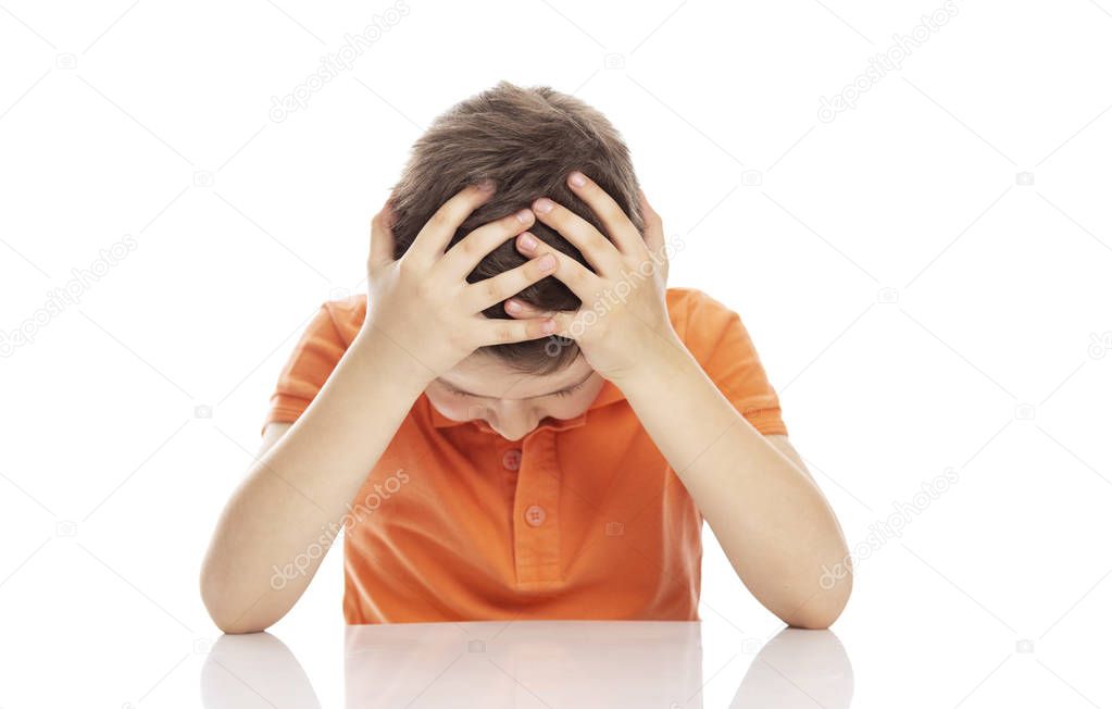 A serious school-age boy in a bright orange polo t-shirt sits at a table, clasping his head in his hands. Despair and lack of help. Close-up. Isolirvoan on a white background.