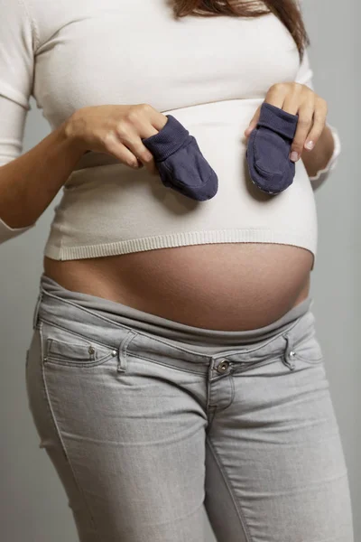 A pregnant woman with a big belly with baby booties in her hands. — Stock Photo, Image