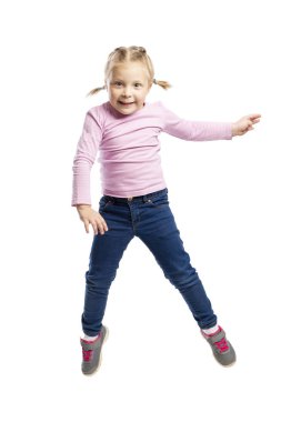 Pembe kazak ve kot pantolonla okul öncesi yaştaki küçük kız zıplıyor. Beyaz arka plan üzerinde yalıtılmış.