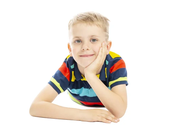 Een school jongen in een heldere gestreepte trui ligt op de vloer en glimlacht. Geïsoleerd over witte achtergrond. — Stockfoto