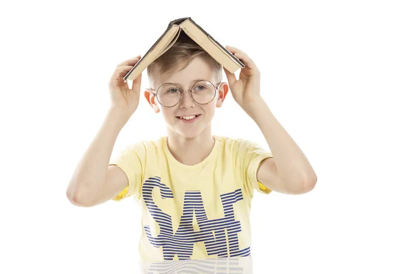 A tinédzser srác a szemüveg egy könyvet a fején a nevetés. Ül az asztalnál. Elszigetelt fehér háttér felett. — Stock Fotó