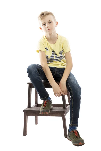 Pantolon ve sarı bir t-shirt pensive adam genç bir sandalyede oturuyor. Beyaz arka plan üzerinde yalıtılmış.