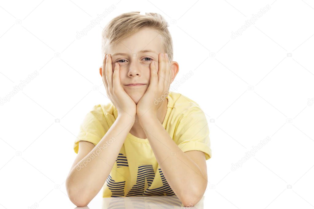 A teenager guy in a yellow T-shirt is sitting at the table, propping his head in his hands. Isolated over white background.