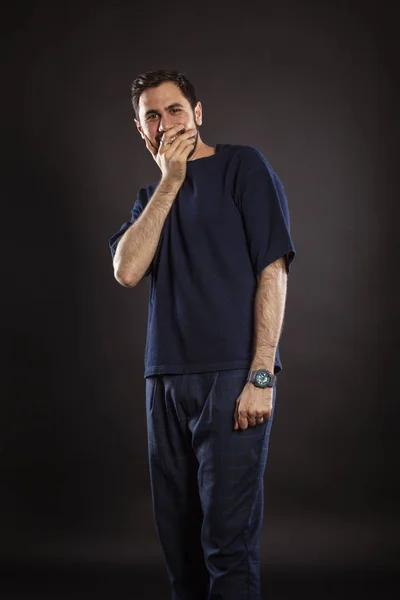 A young handsome man laughs contagiously, covering his mouth with his hand. Black background.