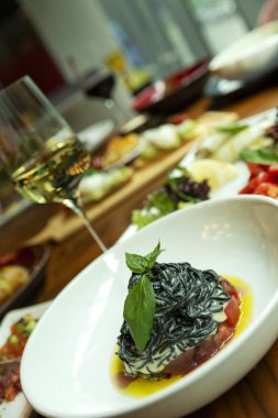 Tabakta balık ve bir kadeh beyaz şarap olan siyah spagetti. Fesleğen yaprağı ile dekore edilmiştir. Close.