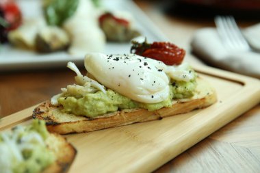 Avokado ile tost üzerine haşlanmış yumurta. Ahşap bir tahtada iştah açıcı bir kahvaltı servis edilmektedir. Close.