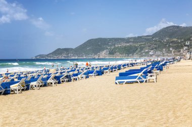 Alanya, Türkiye, 05/07/2019: Güçlü dalgalarla sahilde mavi şezlonglu büyük kumlu plaj.