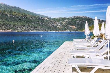 Dağların arasında güzel bir koyda beyaz şezlong ve şemsiye ile lüks plaj. Harika bir manzara. Metin için alan.