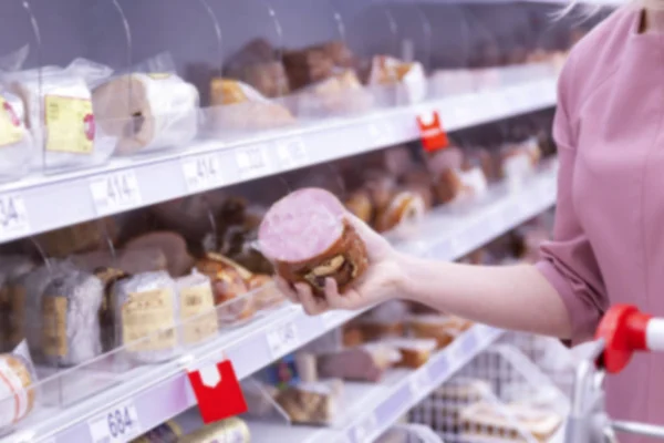 Jovem escolhe salsicha em um supermercado. Borrão . — Fotografia de Stock