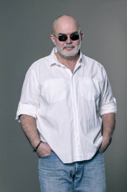 Yaşlı şık kot pantolon ve beyaz gömlek giymiş, gri sakallı kel bir adam.