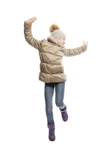 En tonårs flicka i vinterkläder hoppar glatt. Klädd i jeans, stövlar, en varm jacka och hatt. Isolerad över vit bakgrund. — Stockfoto
