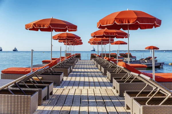 Lüks bir tatil köyünde turuncu şilteli ve şemsiyeli bir sıra iskemle. Güneşli bir gün.